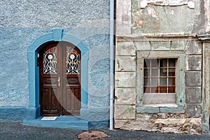 Old and restored nearby. Old wooden door of a shabby demaged house facade. A small town in the mountains of Slovenia