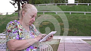 An old retired person uses a tablet computer outdoors. Grandma is learning to use modern digital technologies