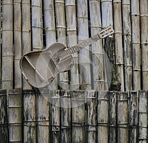 old, retro, aged bamboo fence background. broken abandoned hispanic acoustic Guitar standing on the wall. grunge music