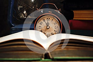 Old retro alarm clock in rustic interior with books and kerosene lamp