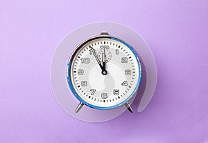 Old retro analog alarm clock in blue on a purple background.