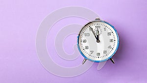 Old retro analog alarm clock in blue on a purple background. The clock starts from five minutes to twelve o`clock. Copy space
