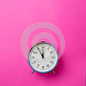 Old retro analog blue alarm clock on a pink background. The clock starts from five minutes to twelve o`clock. Copy space