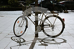 An old retro bicycle stands parked on sidewalk, contrasting shadows of whiles.