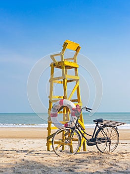 Old retro black bicycle with flowers bouquet beside Life ring for life safety on yellow lifeguard stand station or lifeguard chair