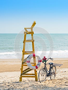 Old retro black bicycle with flowers bouquet beside Life ring for life safety on yellow lifeguard stand station or lifeguard chair