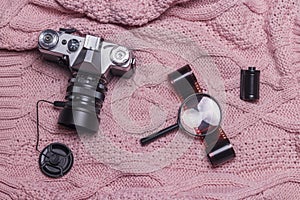 An old retro camera, photographic film and a magnifying glass lie on a pink wool sweater