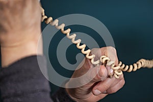 Old retro, old fashioned white telephone cord against green background, woman hand holding telephone cord
