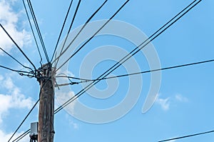 Old retro style wooden pole with many electric supply wires or cables against blue sky