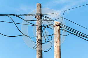 Old retro style wooden pole with many electric supply wires or cables against blue sky