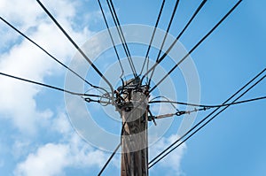 Old retro style wooden pole with many electric supply wires or cables against blue sky