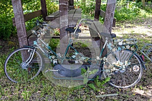 Old retro tandem bicycle adorned with worn plastic flowers, leaning on a wooden hut