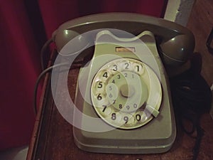 Old retro telephone on a wooden table with red curtain on the background - old photo, vintage style effect