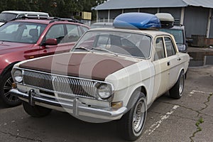 Old retro white GAZ-24 Volga Soviet car with a rusty bonnet parked on a parking lot. Close up corner side view