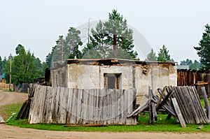 An old, rickety wooden barn stands with an open door behind a fallen fence in the Northern village