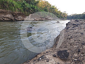 Old river with turbid water flowing alongside are hard rocks