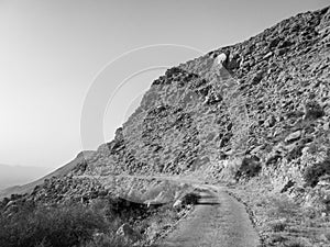 Old road on dry rocky hillside in the desert in black and white