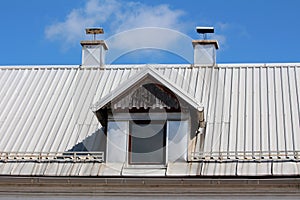 Old roof window with wooden frame and dilapidated decorative boards on top surrounded with two metal sheets covered chimneys