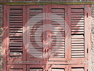 old rose color wooden window with louver panel that peeling and damaged under sunlight