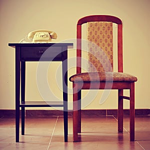 old rotary dial telephone on a table next to a chair, with a retro effect photo
