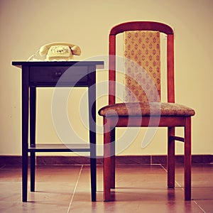 old rotary dial telephone on a table next to a chair, with a retro effect