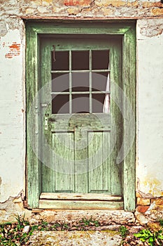An old rotten wooden door on crumbling house. Vintage matte look effect