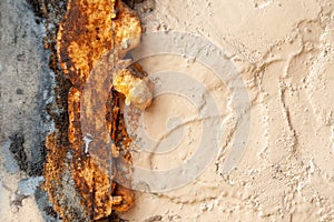 Old rough beige painted wall with cracks and hole, covered with rusty spray foam