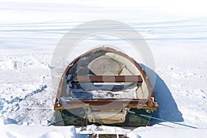 Old rowing boat in the frozen lake on a sunny winter day, concept metaphor for burn out, slow down and standstill in the business