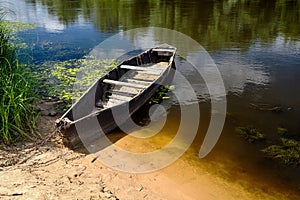 Old rowing boat tied with chain and padlock at green summer bank