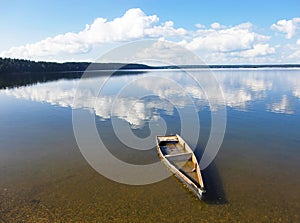 Old rowing boat under water at the shore. The clouds are beautifully reflected in the water. Forsaken broken little craft in a