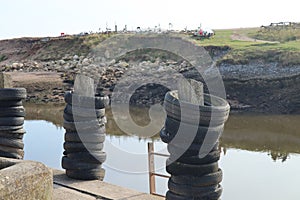 Old rubber tyres stacked up on wooden posts at a mooring spot on the river Axe in Axmouth. The tyres prevent damage to the boats