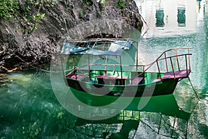 Old rugged green boat docked in the small lake bay
