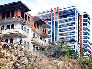 Old ruined house on the background of a new modern house. Facades of old and new houses in one frame. Time contrast