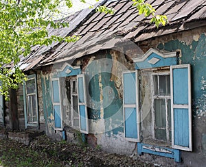 Old ruined house with open window shutters in the village in summer