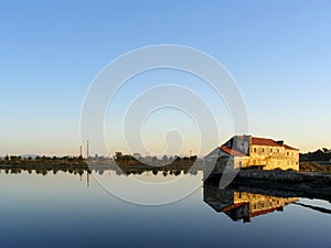 Old ruined Tide Mill and water mirror at Seixal Bay by sunset.