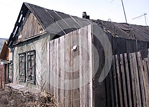 An old ruined wooden house with an uninhabited unnecessary building behind a fence with closed Windows a dilapidated abandoned