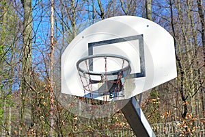 Old run down and rusty basketball basket on play ground surrounded by forest