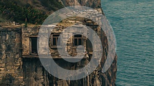 An old rundown house is perched on the edge of a cliff isolated from the bustling city below. The windows are dark and