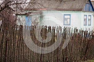 Old rural fence wattle fence made of wooden rods on the background of the house