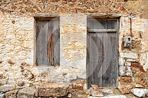 Old rural home facade. Weathered stonewall cottage exterior, wooden brown window and door. Greece