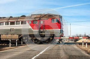 An old russian red train passing across a level crossing, on a small road.