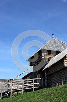 old russian wooden fortress tower with entrance gates and colorful flags on a rope and green grass with blue sky, Torzhok, Russia