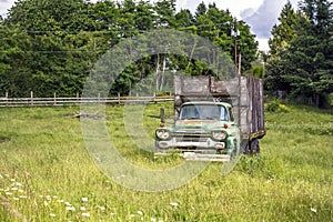 Old rust green truck with wooden trailer standing on the meadow with high grass as a symbol of a past life