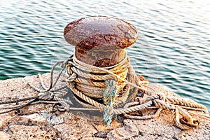 An old and rusted bollard, with several ropes rolled up on itself