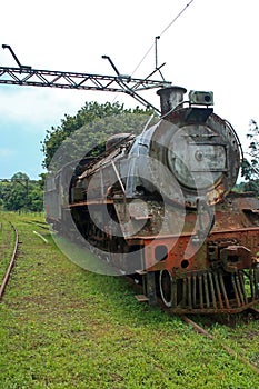 OLD RUSTED STEAM LOCOMOTIVE AT AN ABANDONED STATION WITH OVERHEAD GANTRY