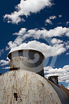 Old rusted tank against a dramatic blue sky.