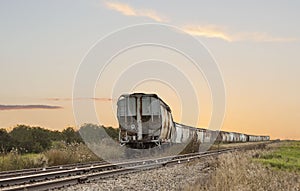 Old rusted train cars sitting on track with sunsetting in background.