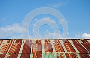 Old rusted and weathered steel quonset hut roof against a blue sky with fluff clouds