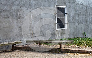 An old rustic alley wall with one solitary barred window.