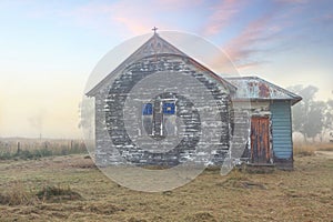 aN old rustic church sits on rural property with a foggy sunrise